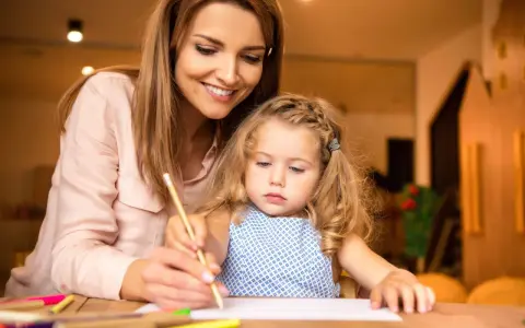 Un educatore professionale guida una bambina nel disegno, con matite colorate sparse sul tavolo.