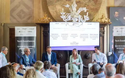 Panel di esperti discute di architetture digitali. Uno dei relatori, con un completo blu, sembra pensare: "non so che lavoro fare".