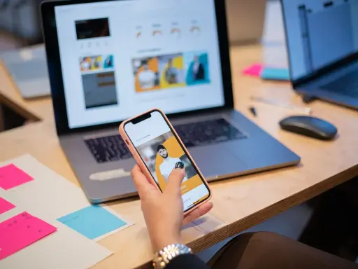 Un ux designer valuta un'interfaccia utente su smartphone, con laptop e post-it colorati sulla scrivania.