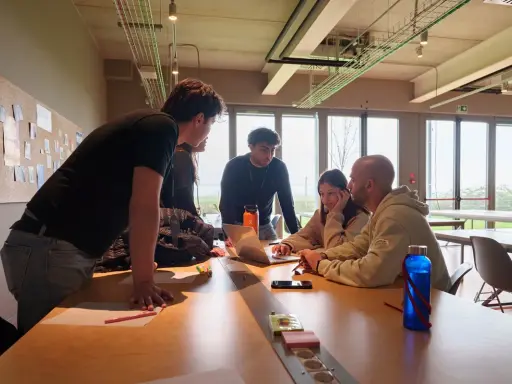 Un gruppo di giovani collabora attorno a un tavolo, un vero team di creator digitale che discute idee davanti a un laptop.