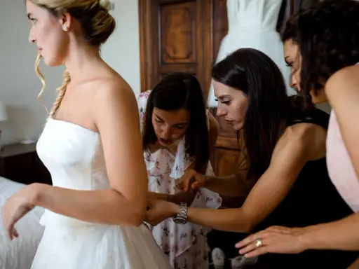 Sposa in abito bianco, aiutata da amiche e forse da una wedding planner, si prepara per il grande giorno.