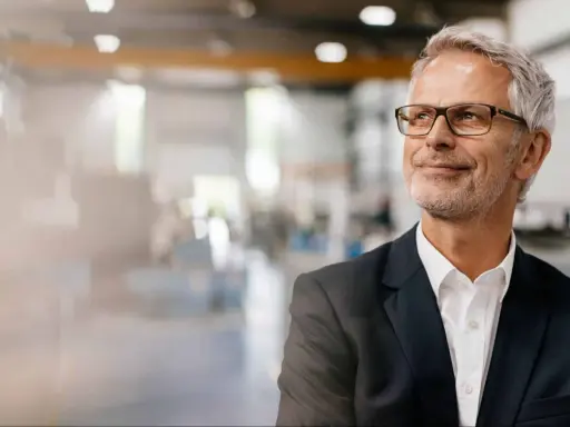 Uomo d'affari con occhiali, sorride guardando in alto, pensando ai suoi prossimi corsi export manager.