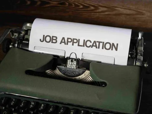 Macchina da scrivere verde con foglio "JOB APPLICATION". Una guida per chi vuole capire come trovare lavoro senza esperienza.