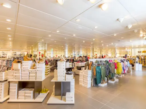 Interno di un negozio di abbigliamento con scaffali pieni di scarpe e vestiti. Un banconista cosa fa? Probabilmente sistema la merce per renderla accattivante.