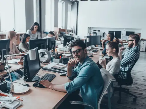 Ufficio moderno con persone al lavoro. Si discute di ccnl grafici editoriali livelli e mansioni, tra scrivanie e computer.