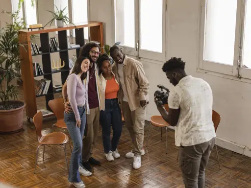 Gruppo di amici sorridenti durante un corso ufficio stampa, uno di loro scatta una foto con il cellulare.