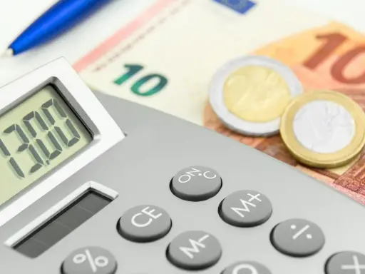 Calcolatrice con display "13.00", banconote da 10 euro e monete. Un promemoria visivo di quando viene pagata la 13esima.