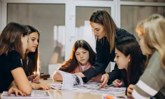 Una pedagogista guida un gruppo di ragazze nello studio, mostrando loro come affrontare un libro.