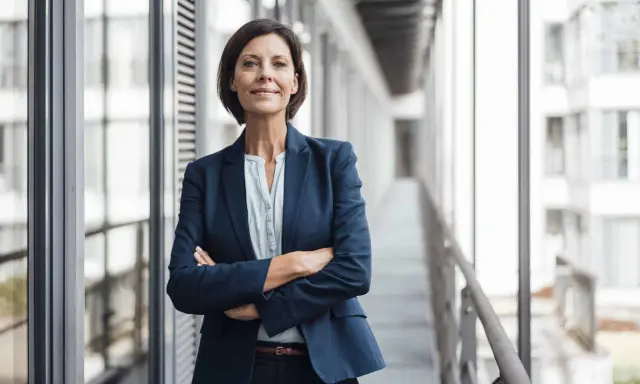 Donna in giacca blu con braccia conserte, sorride. Potrebbe essere un'area manager che discute del suo stipendio.