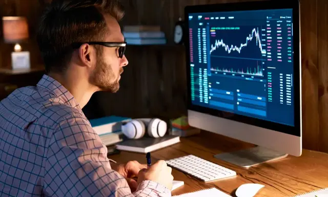 Uomo con occhiali analizza grafici finanziari al computer, comprendendo il broker significato.