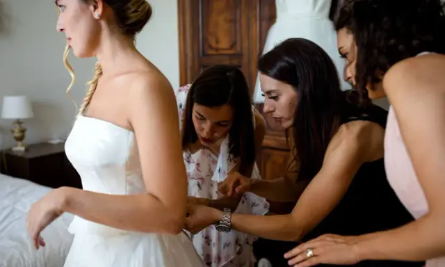 Sposa in abito bianco, aiutata da amiche e forse da una wedding planner, si prepara per il grande giorno.