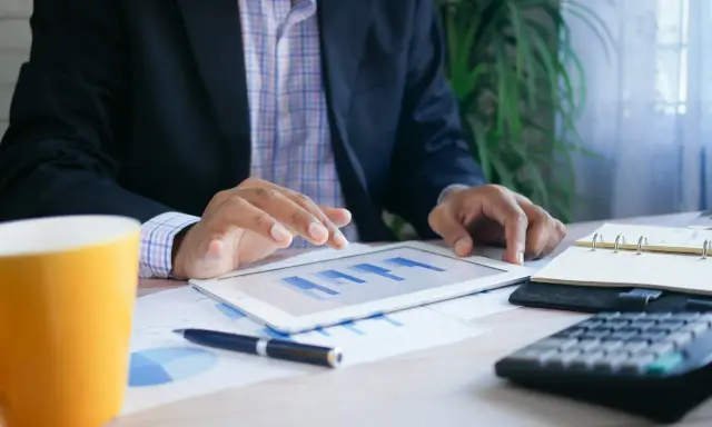 Uomo d'affari analizza grafici su tablet, con tazza, calcolatrice e agenda. Un esempio di come trovare lavoro a 60 anni con nuove competenze.