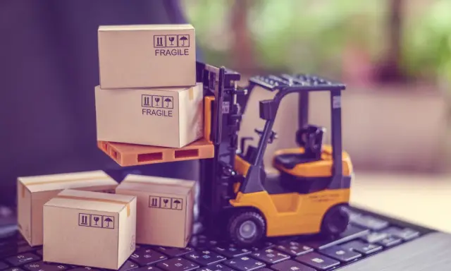 Carrellino elevatore giallo solleva scatole fragili su un pallet, mentre altre scatole attendono su una tastiera. Il buyer cosa fa? Organizza la spedizione.