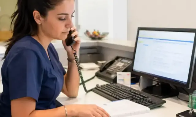 Impiegata studio medico al telefono, consulta un registro e il computer per gestire appuntamenti e richieste.