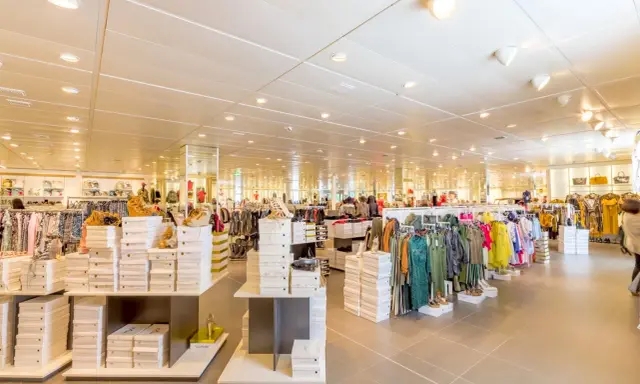 Interno di un negozio di abbigliamento con scaffali pieni di scarpe e vestiti. Un banconista cosa fa? Probabilmente sistema la merce per renderla accattivante.
