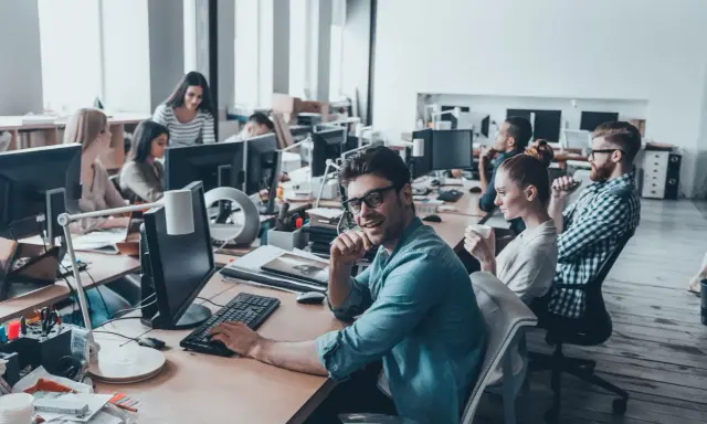 Ufficio moderno con persone al lavoro. Si discute di ccnl grafici editoriali livelli e mansioni, tra scrivanie e computer.