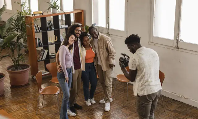Gruppo di amici sorridenti durante un corso ufficio stampa, uno di loro scatta una foto con il cellulare.
