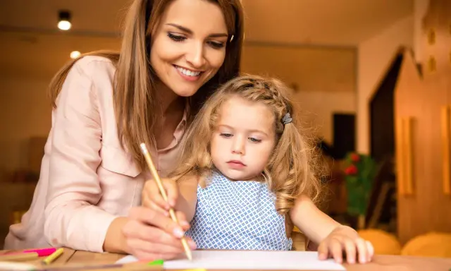Un educatore professionale guida una bambina nel disegno, con matite colorate sparse sul tavolo.