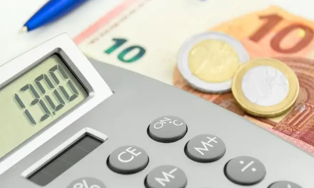 Calcolatrice con display "13.00", banconote da 10 euro e monete. Un promemoria visivo di quando viene pagata la 13esima.