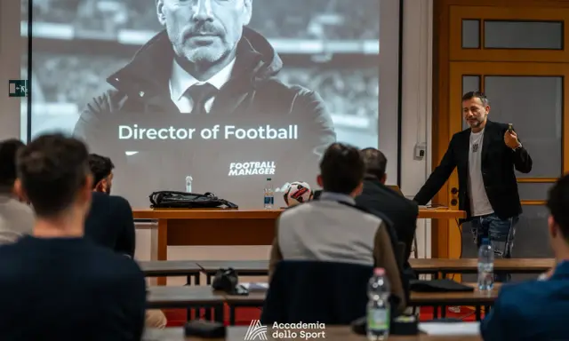 Un relatore parla a un pubblico interessato, con una proiezione che mostra "Director of Football". Un corso per chi vuole lavorare nel calcio.