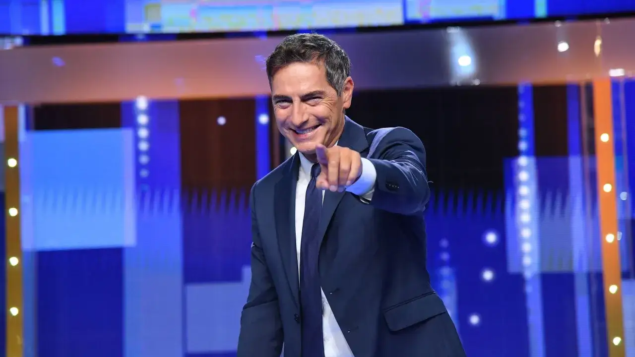 Un uomo sorridente in giacca blu indica lo spettatore, un invito a scoprire come iniziare una presentazione con energia.