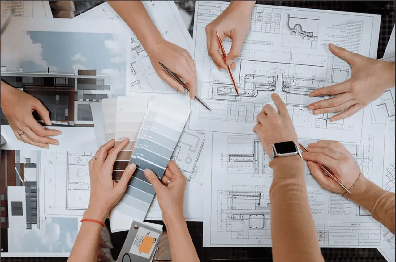 Mani che esaminano progetti e campioni di colore, discutendo quanto guadagna un interior designer.