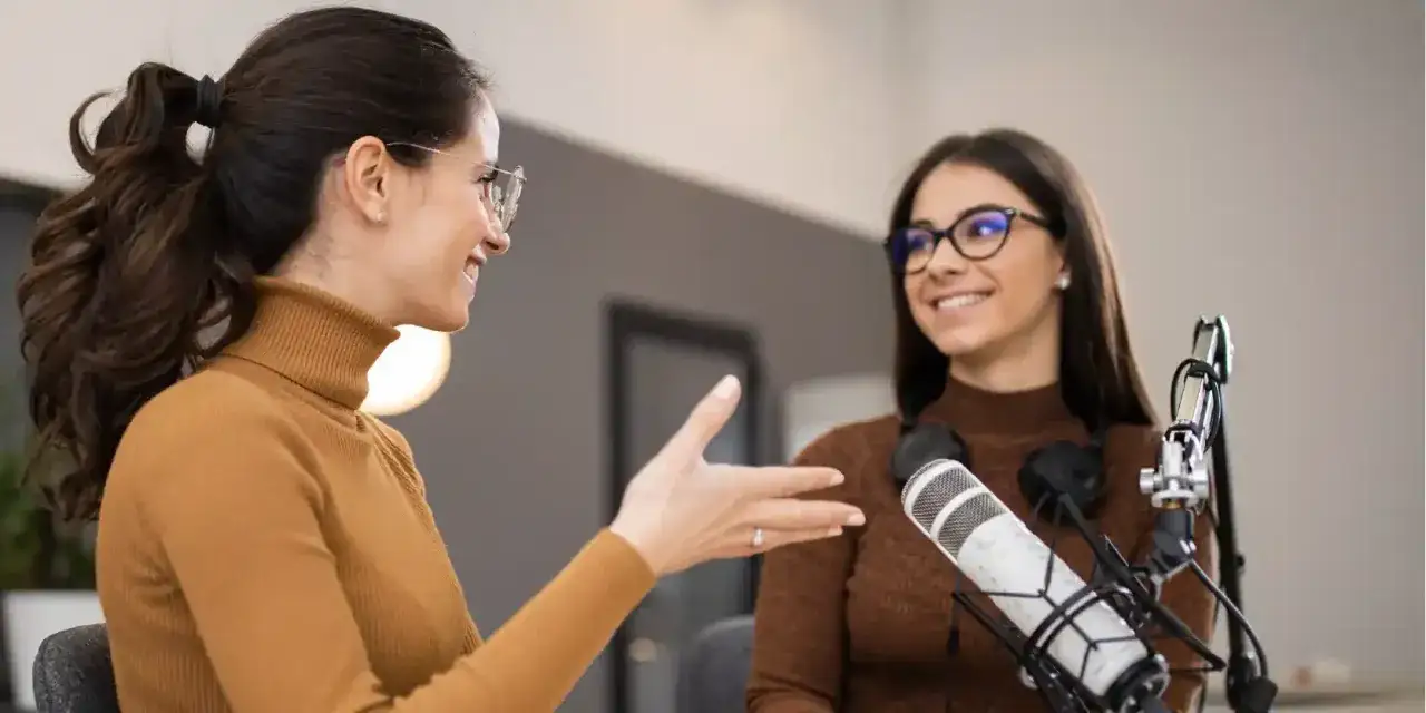 Due donne con microfoni discutono, i loro toni di voce creano un'atmosfera coinvolgente per il podcast.