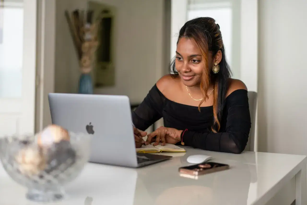 Ragazza sorridente studia al computer, prendendo appunti. Un'opportunit&agrave; per un corso di inglese gratuito.