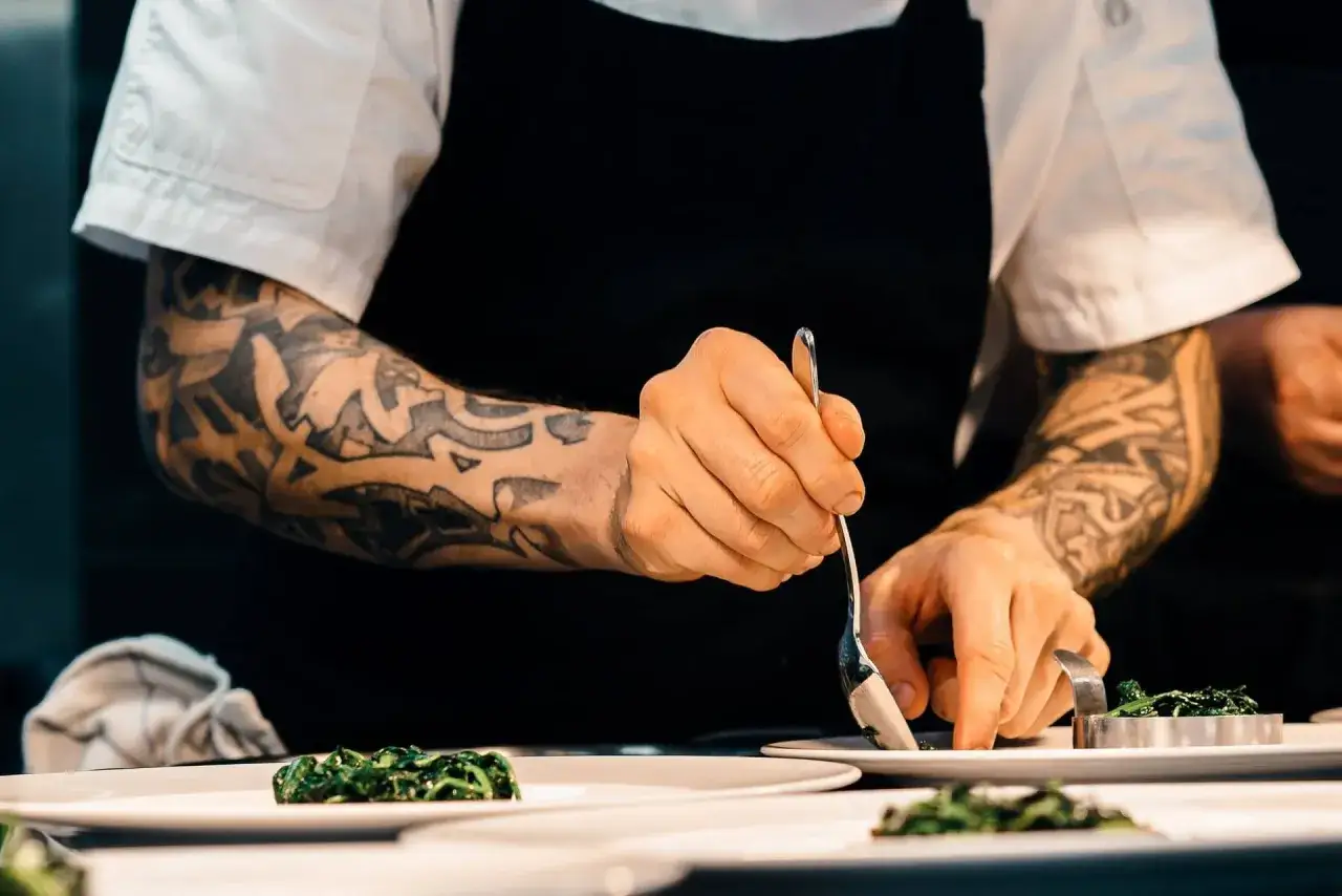 Cuoco con tatuaggi prepara un piatto. Quanto guadagna un cuoco? Dipende dall'esperienza e dal ristorante.