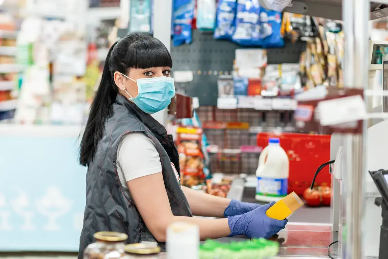 Cassiera con mascherina e guanti in un supermercato, mentre passa un prodotto al nastro. La GDO, grande distribuzione organizzata, &egrave; questo: un luogo di acquisto quotidiano.