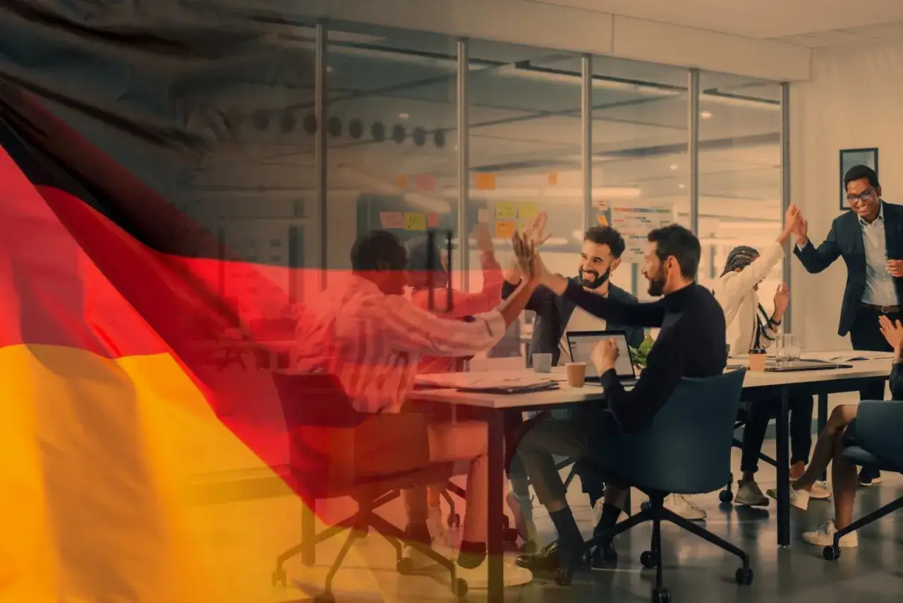 Team di successo celebra in ufficio, con la bandiera tedesca sovrapposta. Opportunit&agrave; di offerte di lavoro in Germania senza lingua tedesca.