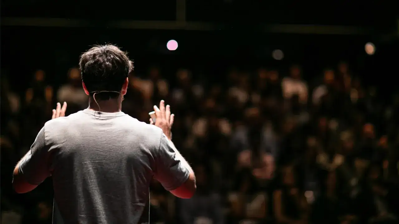 Un relatore, con un microfono dietro l'orecchio, si rivolge a un pubblico numeroso. &Egrave; il momento del suo breve discorso di saluto.
