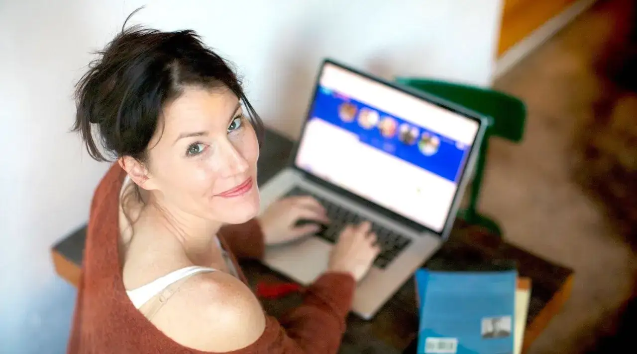 Donna sorride mentre digita al computer, forse sta seguendo un inglese corso gratis per migliorare le sue competenze.