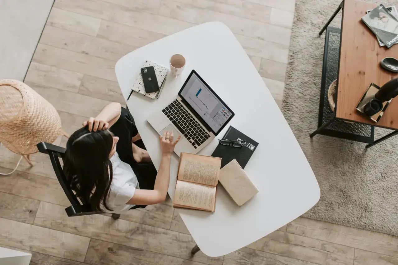 Donna lavora al computer, con libri e quaderni sul tavolo. Un ambiente ideale per il suo secondo lavoro da casa.