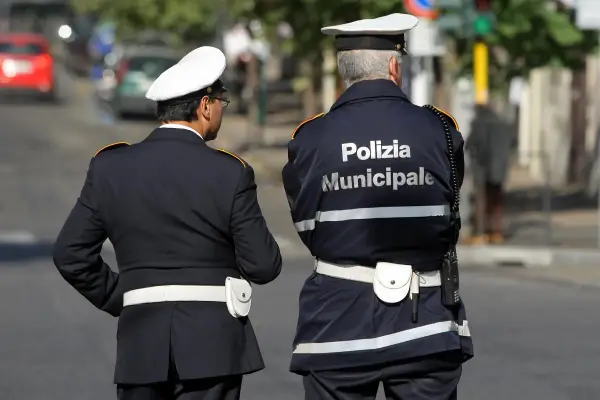 Due vigili urbani in divisa, uno con la scritta "Polizia Municipale" sulla schiena, in attesa di un equo stipendio.