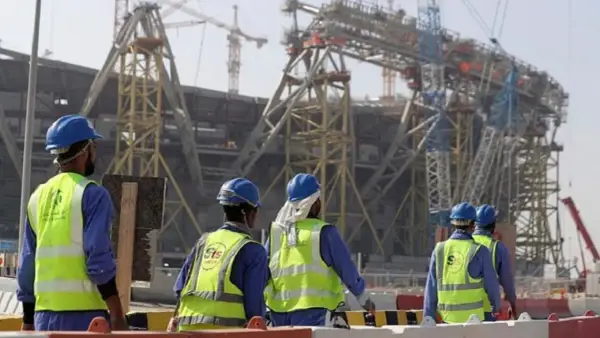 Operai con caschi e giubbotti ad alta visibilità lavorano in Qatar alla costruzione di un imponente stadio.